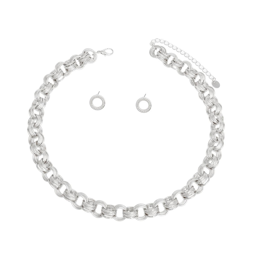 Overhead flat lay of a chunky silver rhodium tone triple ring rolo chain choker necklace arranged in a circle on a white background. Each link features three interlocking rings with two polished and one ribbed textured ring. A lobster clasp closure and 3-inch extender chain with small oval links and a round hang tag are visible at the top. Two small open circle ring stud earrings with ribbed texture and post backings are displayed inside the necklace loop.