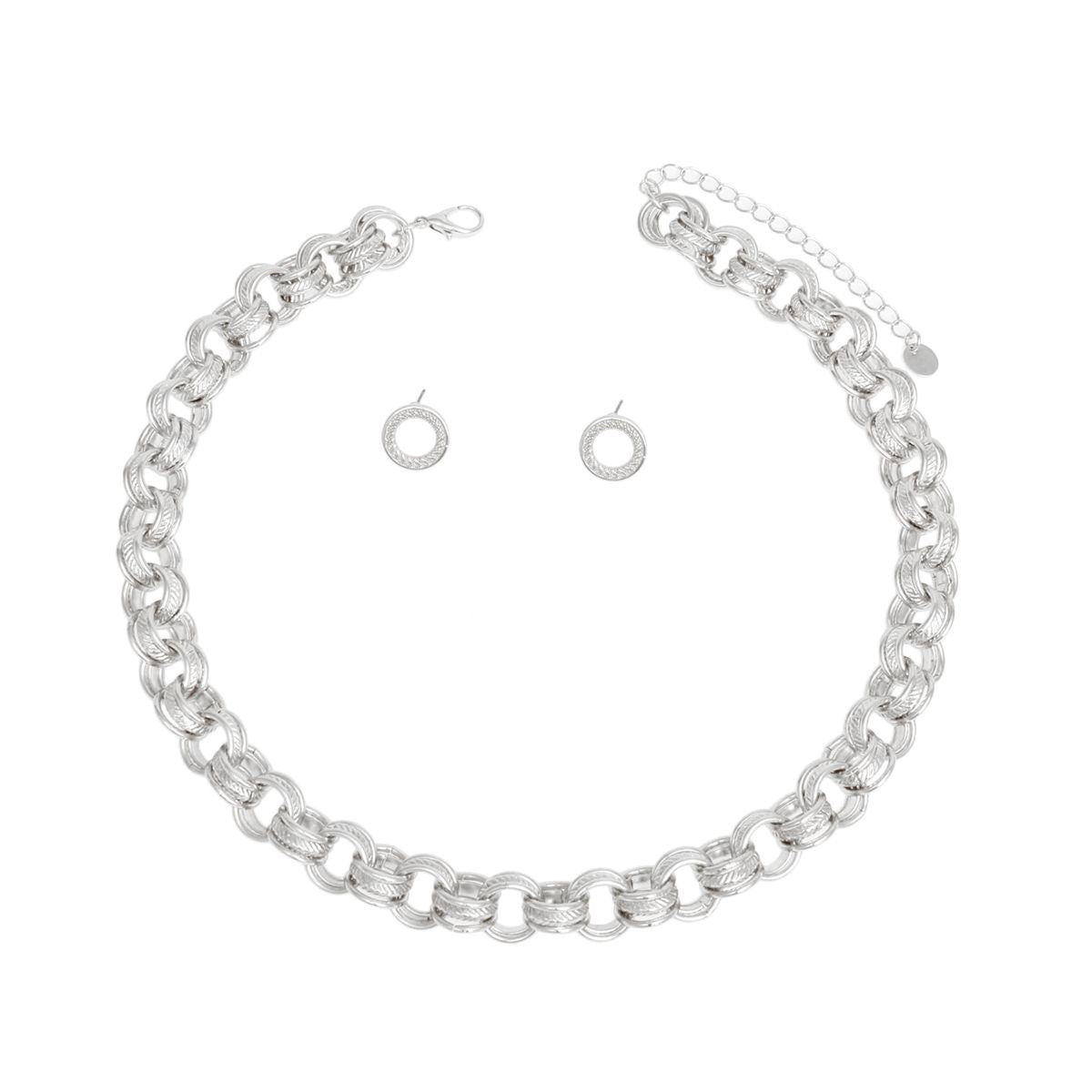 Overhead flat lay of a chunky silver rhodium tone triple ring rolo chain choker necklace arranged in a circle on a white background. Each link features three interlocking rings with two polished and one ribbed textured ring. A lobster clasp closure and 3-inch extender chain with small oval links and a round hang tag are visible at the top. Two small open circle ring stud earrings with ribbed texture and post backings are displayed inside the necklace loop.