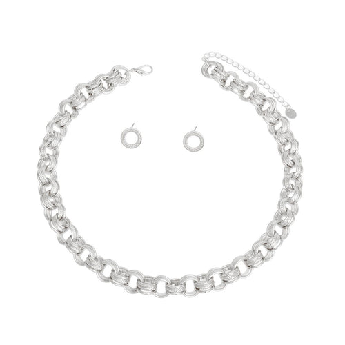 Overhead flat lay of a chunky silver rhodium tone triple ring rolo chain choker necklace arranged in a circle on a white background. Each link features three interlocking rings with two polished and one ribbed textured ring. A lobster clasp closure and 3-inch extender chain with small oval links and a round hang tag are visible at the top. Two small open circle ring stud earrings with ribbed texture and post backings are displayed inside the necklace loop.