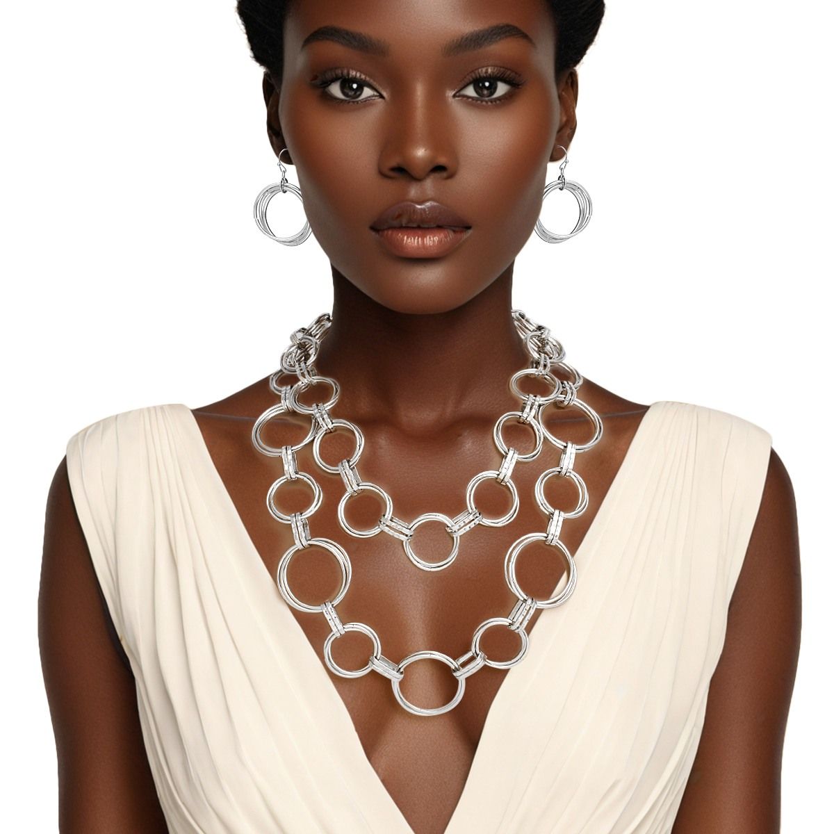 Woman wearing the double layer chunky silver ring link necklace draped over chest, paired with matching circular hoop-style fish hook earrings, styled with a cream deep V-neck sleeveless dress, white background