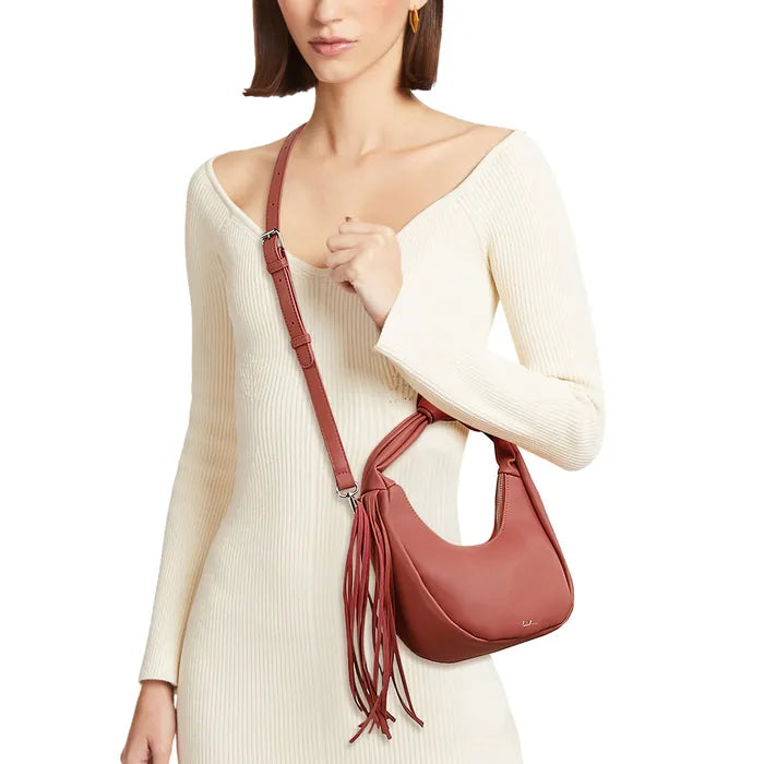 Model in a cream ribbed dress wearing a blush pink crescent bag crossbody, with a knotted handle and long side fringe