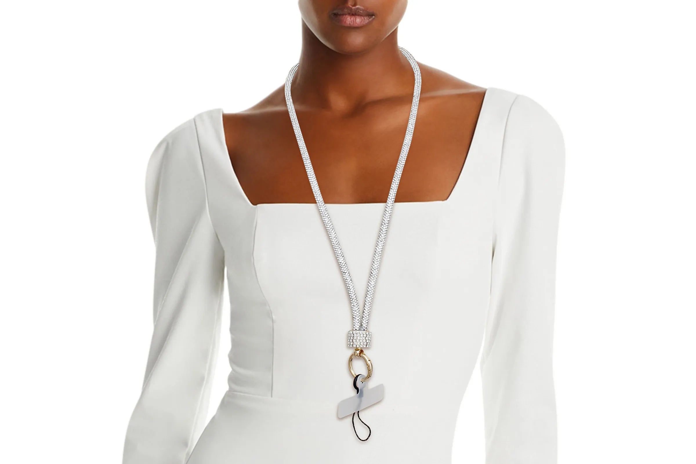 Black woman wearing clear rhinestone-encrusted tube phone lanyard around neck over white square-neck dress, with clear rhinestone barrel slide, round gold push clasp, black jump ring, and clear plastic card insert hanging at chest level