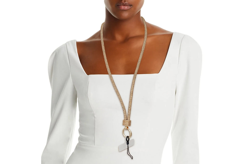 Black woman wearing topaz gold rhinestone-encrusted tube phone lanyard around neck over white square-neck dress, with gold push clasp, black jump ring, and clear plastic card insert hanging at chest level
