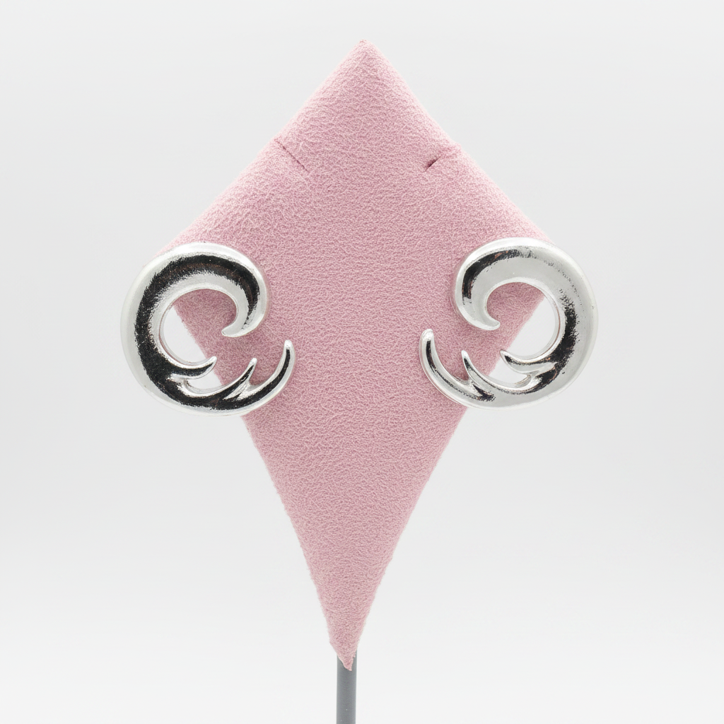 Pair of bold silver spiral swirl stud earrings displayed on pink diamond-shaped suede jewelry stand, pure white background, showing chunky open spiral swirl design in high-polish silver-tone metal