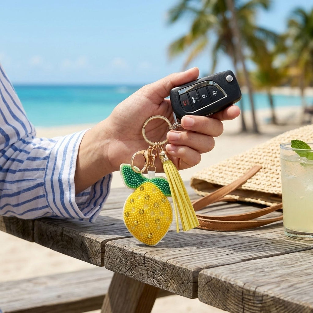 Yellow and green seed bead lemon charm keychain with yellow faux leather tassel and gold lobster clasp, held with a car key fob at a tropical beach setting