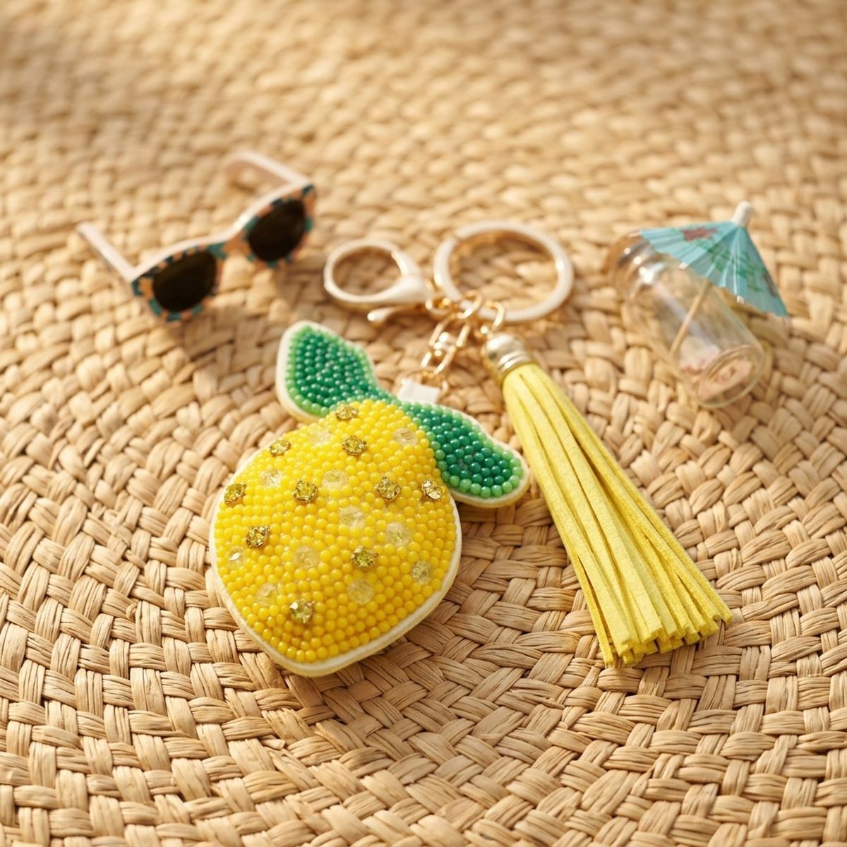 Yellow and green seed bead lemon charm keychain with rhinestone accents and yellow faux leather tassel, styled on wicker surface with sunglasses and cocktail umbrella