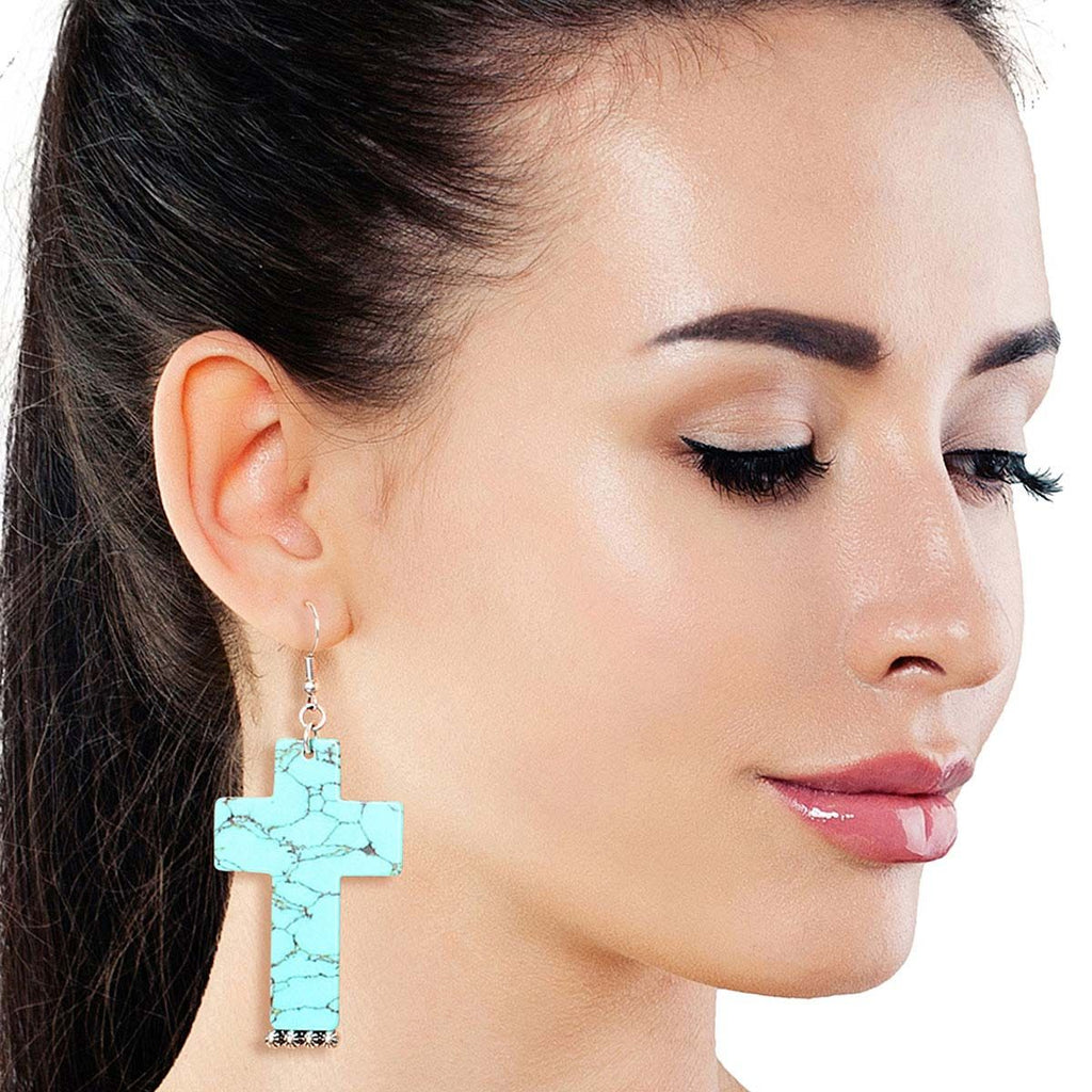 Close-up of a woman wearing a turquoise marbled acrylic cross drop earring with silver-tone fish-hook hardware against a white background.