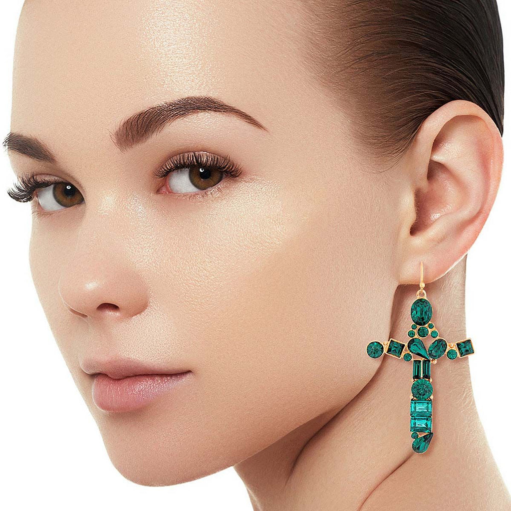 Model wearing a gold-tone cross drop earring with emerald-green mixed-cut crystals and a slim fishhook against a white background